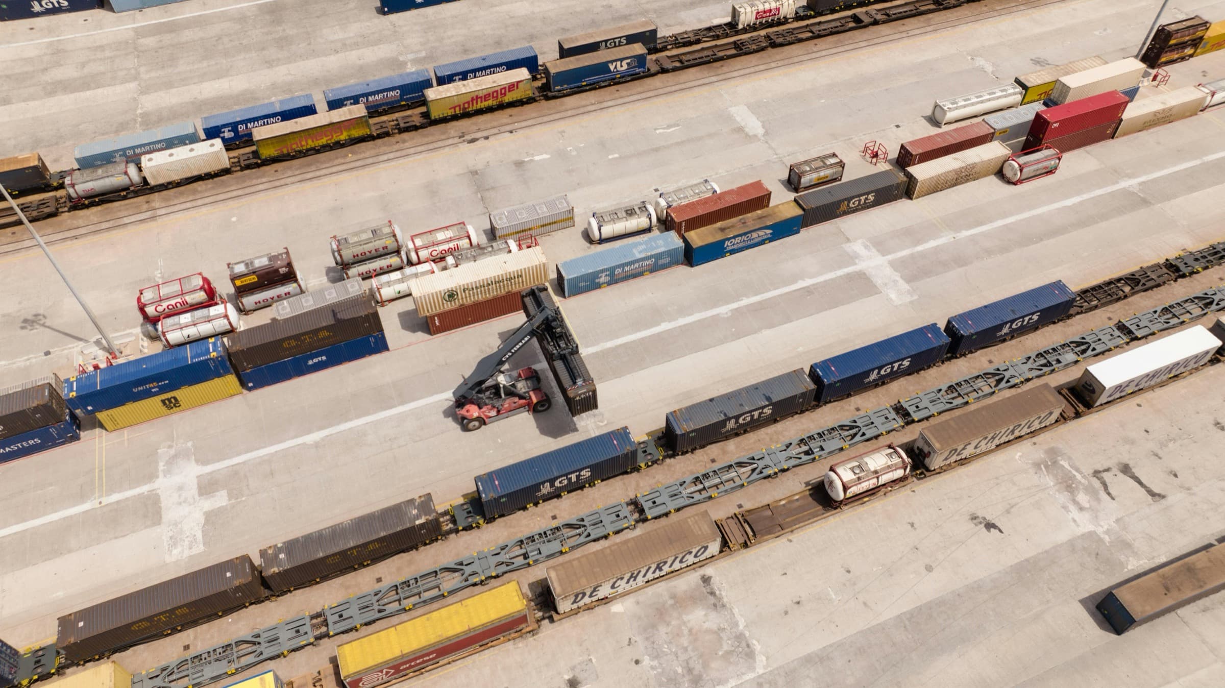 Terminal intermodal văzut de sus, cu containere pe vagoane platformă și un reach stacker.